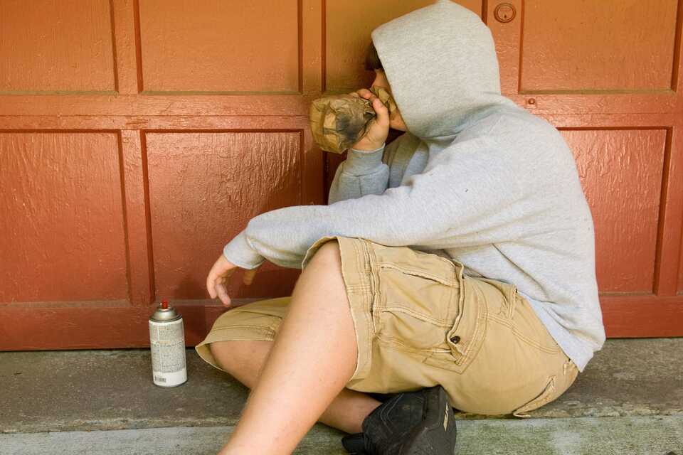 Persona inhalando químicos desde una bolsa de papel